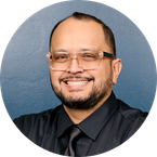 Juan wearing glasses and black button up with tie