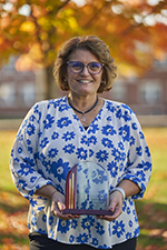 Woman smiling and holding plaque outside on a beautiful fall day
