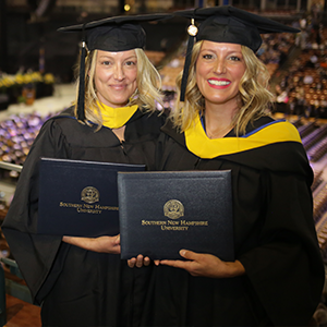 Two people in graduation regalia holding diploma