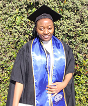 Consolee Amina poses in her commencement regalia in front of a very green bush