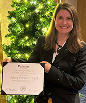 Woman holding certificate and smiling in front of a lit holiday tree